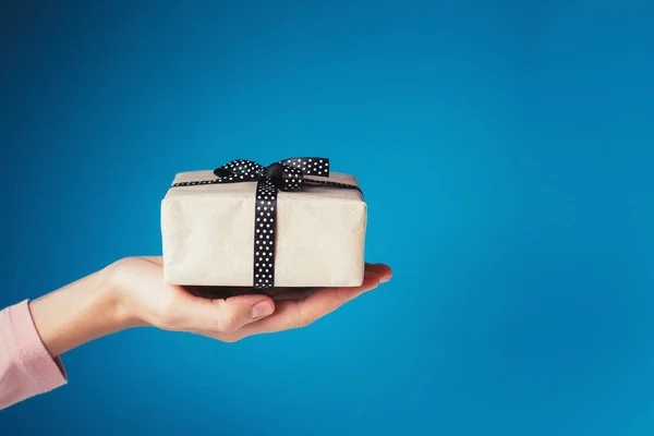 Donna mano tiene scatola regalo su palmo su sfondo blu con spazio copia — Foto Stock