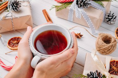 Noel süslemeleri hediye kutuları, çam kozalakları ve kadın çay beyaz ahşap zemin üzerinde eller