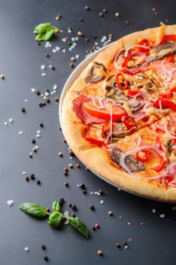 İtalyan pizza ve taze fesleğen yaprakları koyu bir kağıt üzerinde yarısı kadar yakın. Geleneksel İtalyan mutfağı