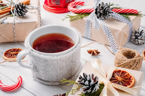 Рождественские украшения с подарочными коробками, шишками и чашкой чая на белом деревянном фоне — стоковое фото