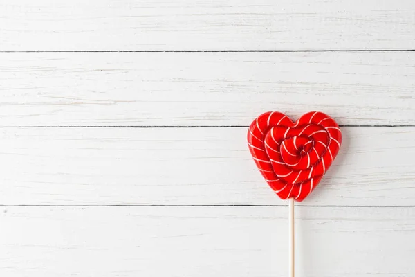Red lollipop in shape of heart on a white wooden background