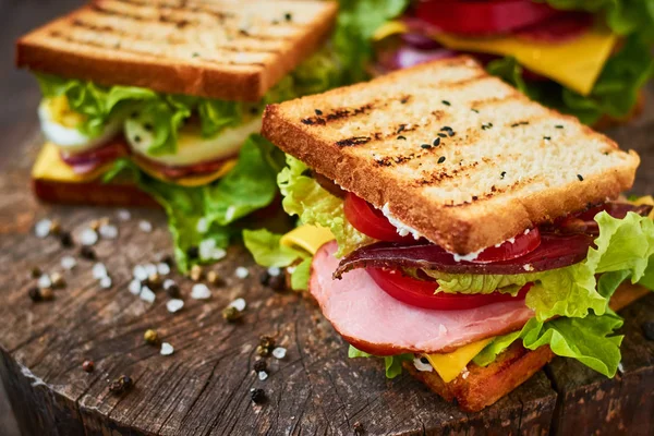 Домашний сэндвич с ветчиной, салатом, сыром и помидорами на деревянном фоне — стоковое фото