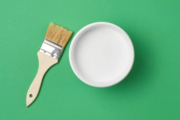 Cepillo y lata de pintura con color blanco sobre un fondo verde, vista superior — Foto de Stock