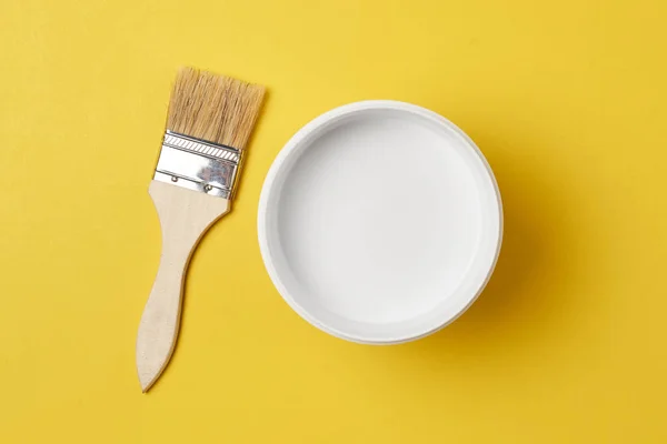 Cepillo y lata de pintura con color blanco sobre un fondo amarillo, vista superior — Foto de Stock