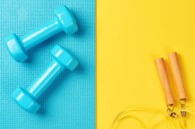 Düz, üstten görünüm en az arka plan, fitness kavramı yatıyordu. Mavi dumbell ve mavi ve sarı zemin üzerine ip atlama