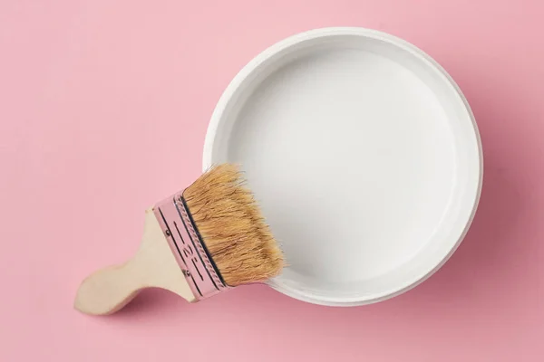 Pensel och färg kan med vit färg på en rosa bakgrund, ovanifrån — Stockfoto