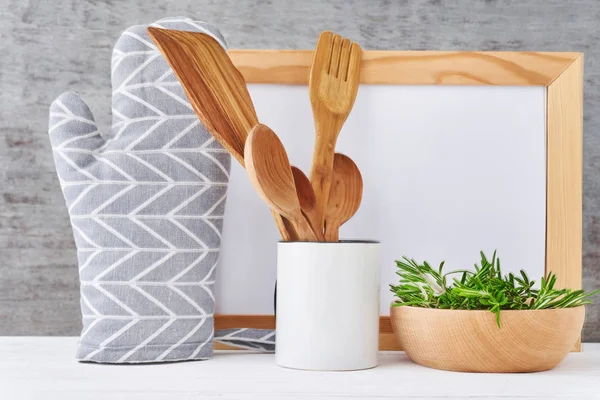 Fondo de utensilios de cocina con papel blanco vacío, cubiertos de madera y agarradera sobre una mesa blanca — Foto de Stock