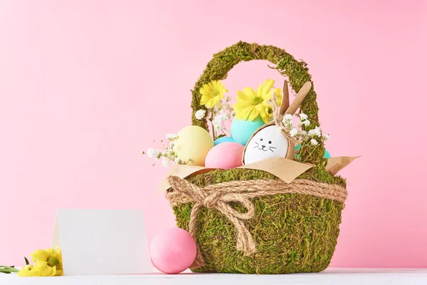 Conceito de Páscoa. Ovos de Páscoa em cesta decorativa com flores em um fundo rosa — Fotografia de Stock