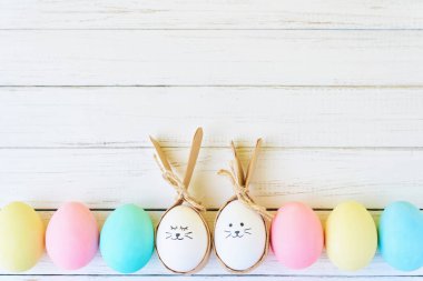 Boyalı yüzler ve tavşan kulakları satırındaki beyaz bir arka plan üzerinde renkli Paskalya yumurtaları