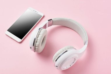 Beyaz kablosuz kulaklık ve pastel pembe bir arka plan üzerinde smartphone