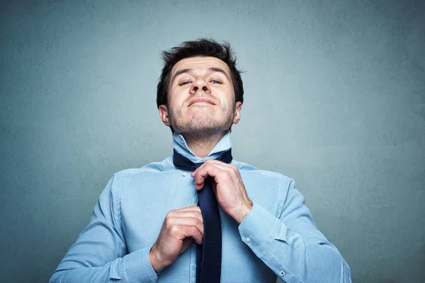 Hombre con camisa ata una corbata con emoción sobre un fondo gris — Foto de Stock