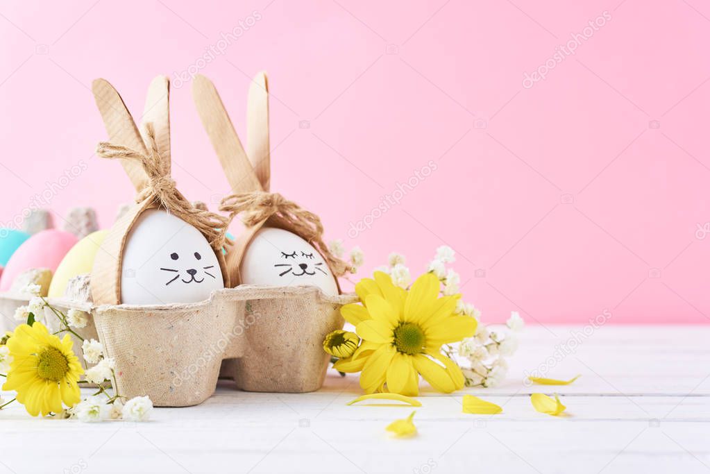 Easter colored eggs with painted faces in paper tray with decorationd on a pink background