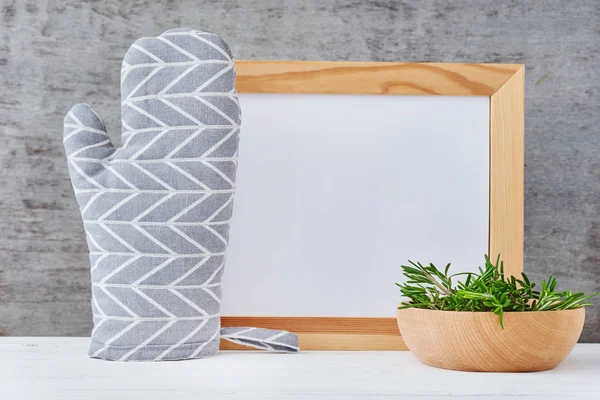 Utensilios de cocina fondo con papel blanco vacío, agarradera y tazón con romero sobre una mesa blanca — Foto de Stock