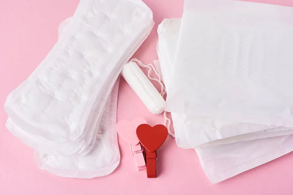 Pad sanitasi, tampon menstruasi dan hati merah kayu pada latar belakang merah muda, top view — Stok Foto