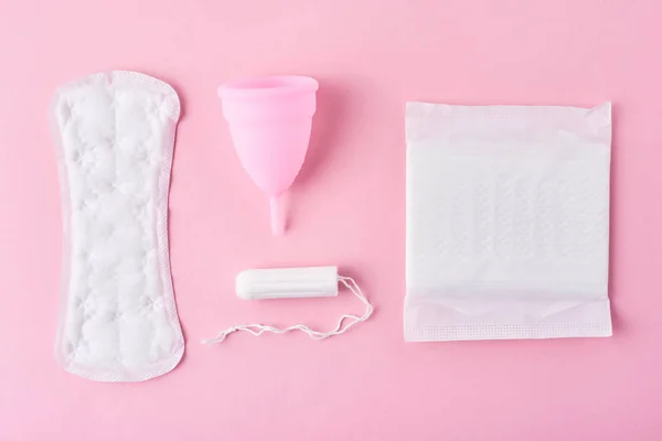 Санітарна подушка, менструальна чашка і тампон на рожевому фоні, вид зверху — стокове фото