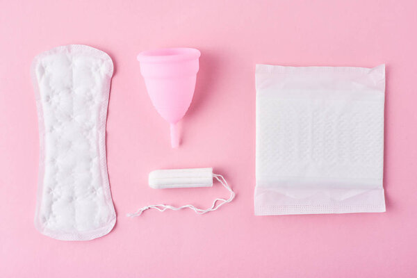 Sanitary pad, menstrual cup and tampon on a pink background, top view