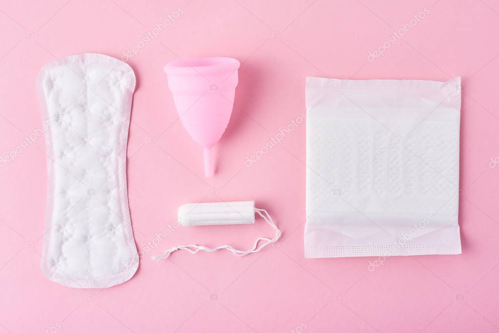 Sanitary pad, menstrual cup and tampon on a pink background, top view