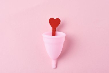 pembe arka planda menstrüel fincan ve kırmızı ahşap kalp