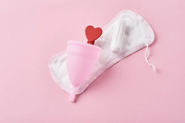 Pad sanitasi, cangkir menstruasi, tampon dan hati kayu merah pada latar belakang merah muda — Stok Foto