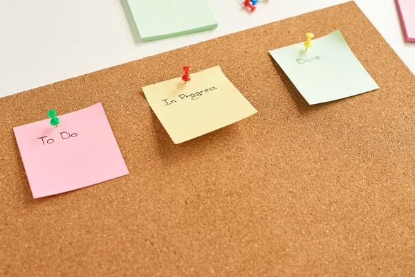 五颜六色的纸笔记, 上面钉着 "要做"、"正在进行" 和 "完成" 两个字, 固定在软木塞板上 — 图库照片