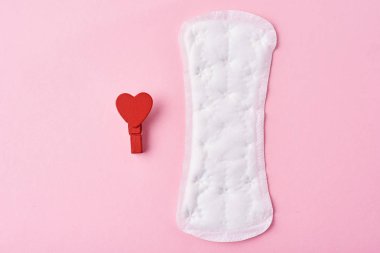 Hijyenik ped ve pembe bir arka plan üzerinde kırmızı ahşap kalp