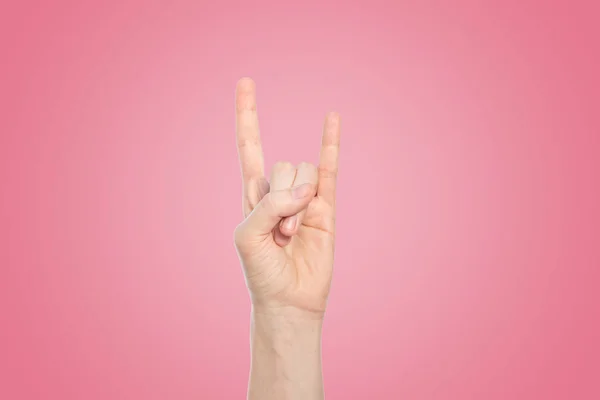 Hand show rock gesture on a pink background, close up.