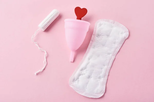 Sanitary pad, menstrual cup, tampon and red wooden heart on a pink background — Stock Photo, Image