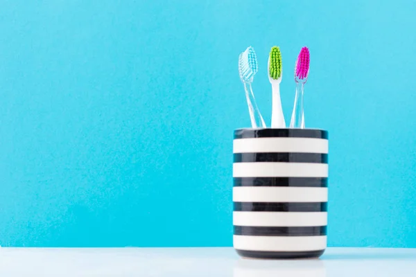 Three plastic colorful toothbrushes in glass on a blue background, close up — Stock Photo, Image