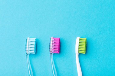 Mavi arka plan üzerinde üç plastik renkli diş fırçaları, yakın
