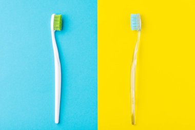 Pastel mavi ve sarı arka plan üzerinde iki plastik diş fırçası
