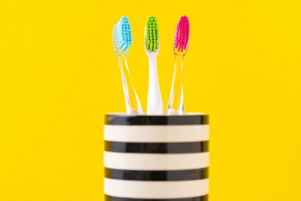 Tres coloridos cepillos de dientes de plástico en vidrio sobre un fondo amarillo, de cerca — Foto de Stock