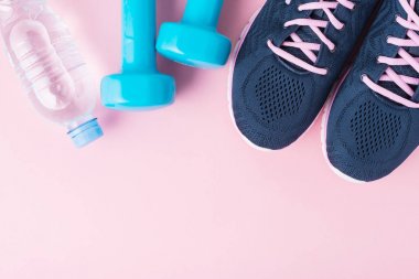 Kadın spor ayakkabı, mavi halter ve kopya alanı ile pembe bir arka plan üzerinde su şişesi, üst görünümü