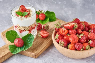 Cam kavanozda yaz çilek ve gri bir arka plan üzerinde ahşap kase taze çilek ile Smoothie