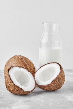 Cam şişede hindistan cevizi sütü ve gri arka planda taze hindistan cevizi.