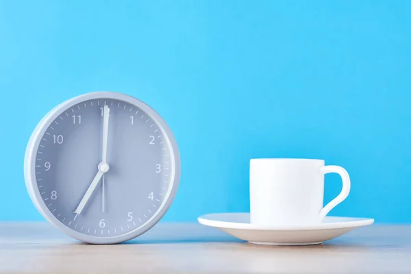 Klasické šedé výstražné hodiny a bílý šálek kávy na modrém pozadí — Stock fotografie