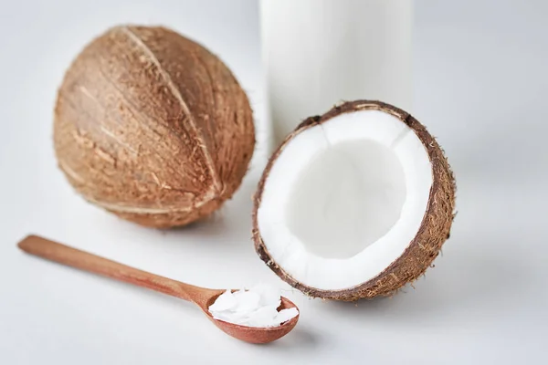 Coconut milk in glass bottle and fresh coconuts with half on a gray background