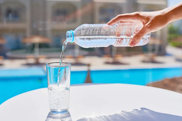 Vrouw hand gieten water in een glas van plastic fles Temp zwembad achtergrond — Stockfoto