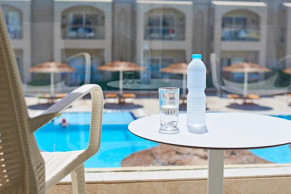 Glass of water and plastic bottle on a balcony against swimming