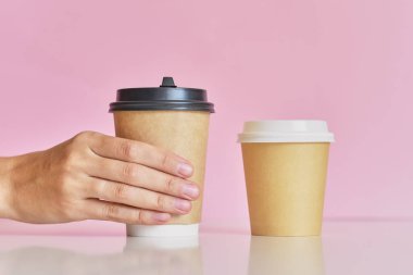 Kadın el pembe arka plan üzerinde iki kahve kağıt fincan almak