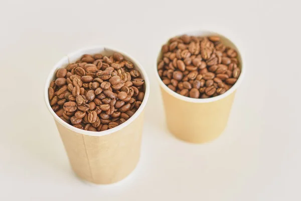 Две бумажные чашки кофе с кофейными зернами на белом фоне — стоковое фото