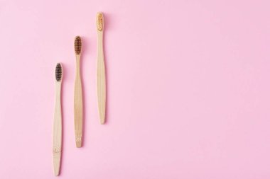 pembe bir arka plan üzerinde üç ahşap bambu diş fırçaları, üst görünümü.