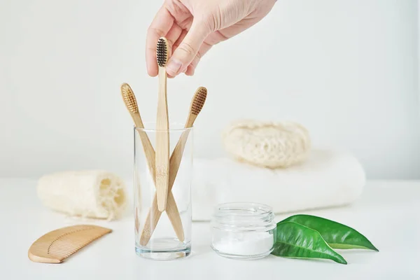 Woman hand take wooden bamboo toothbrush in a bathroom interior. — Stock Photo, Image