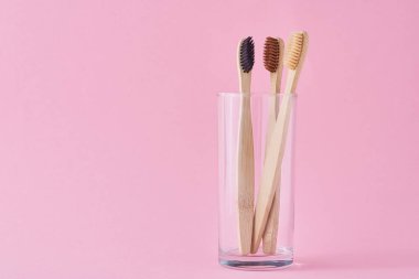 Pembe arka planda camda üç tahta bambu diş fırçası.. 