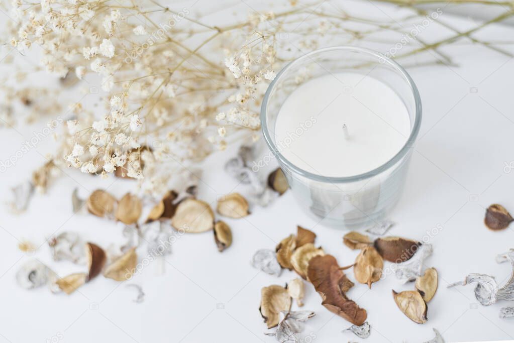 Candle with floral decor on a white table. Cozy and hygge backgr