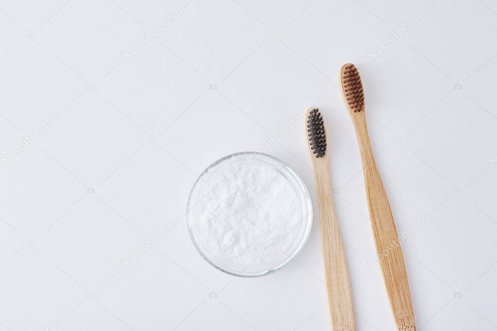 Two wooden bamboo toothbrushes and baking soda powder in glass j