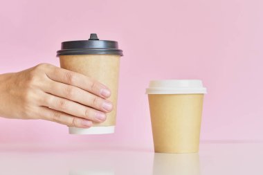 Kadın el pembe arka plan üzerinde iki kahve kağıt fincan almak