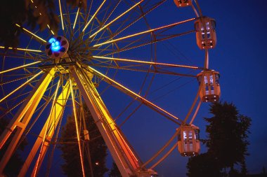 Bir gece şehrindeki lunaparkta yanan dönme dolap.