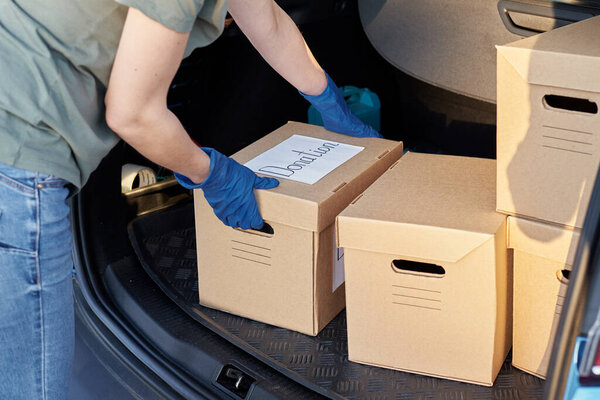 Donation and volunteering concept. Woman in gloves load box in car trunk.