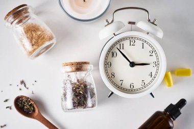 Depresyon ve uykusuzluk tedavisi için bitkisel ilaçlar. Alarm saati, şifalı bitkiler ve beyaz arka planda aromaterapi yağı.