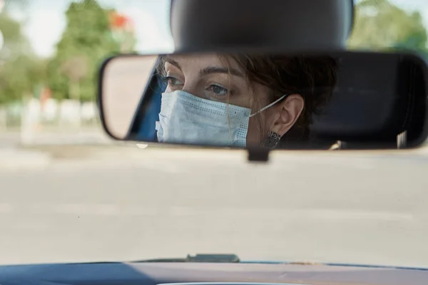 reflection of woman in protective medical mask in the rear view mirror in car. Virus protection and healt care concept